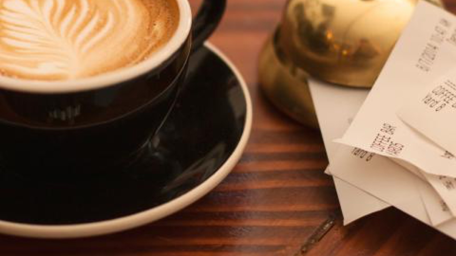 Tazza di cappuccino su un tavolo di legno accanto a un mazzetto di scontrini